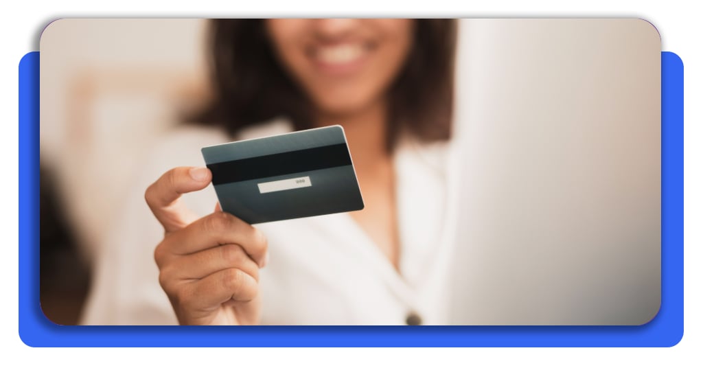 ¿Tarjeta de crédito? Mira si calificas gratis en 1 minuto 6 Una dama sosteniendo una tarjeta de crédito cerca de una laptop como indicativo de las ventajas de obtener este producto financiero.