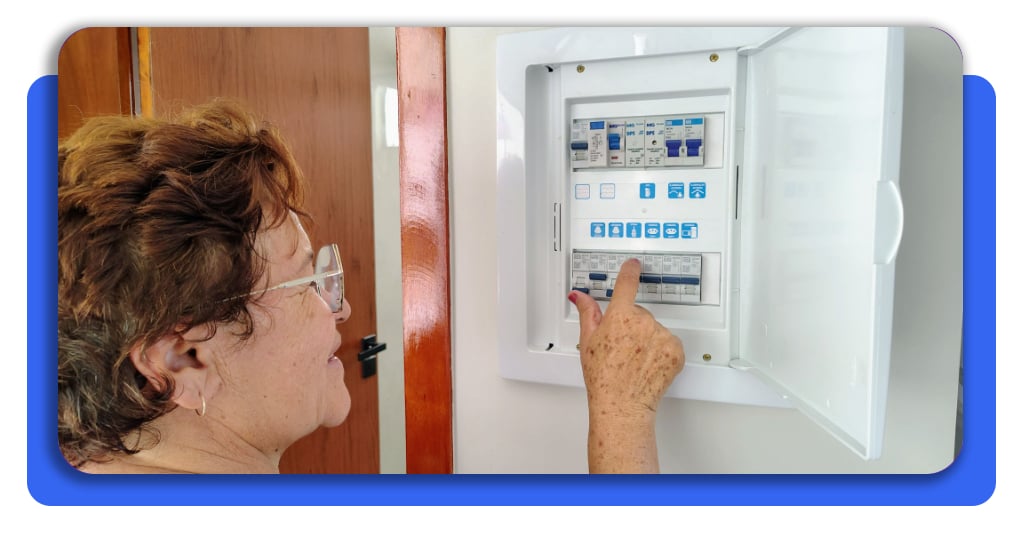 Problemas eléctricos en casa: señales que debes detectar a tiempo 4 Una mujer mayor se encuentra revisando el panel eléctrico de su casa para verificar que se encuentra en buenas condiciones. El espacio luce iluminado.