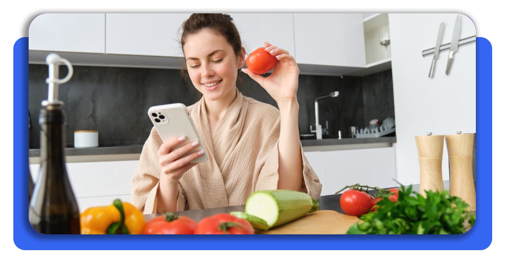 Cómo comer bien toda la semana gastando menos dinero 3 Mujer planificando su menú semanal en la pantalla de un teléfono con verduras a un lado